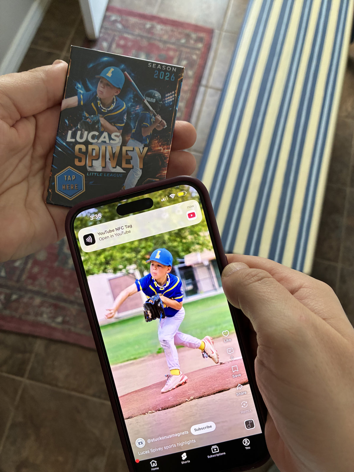 A person holds a custom-made baseball trading card magnet in one hand and a smartphone in the other, showing a video of the young player on the screen.